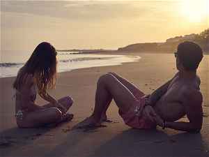 Two people sitting on a beach at sunset