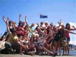 A group of travellers posing with hands in the air and an australian flag in the background